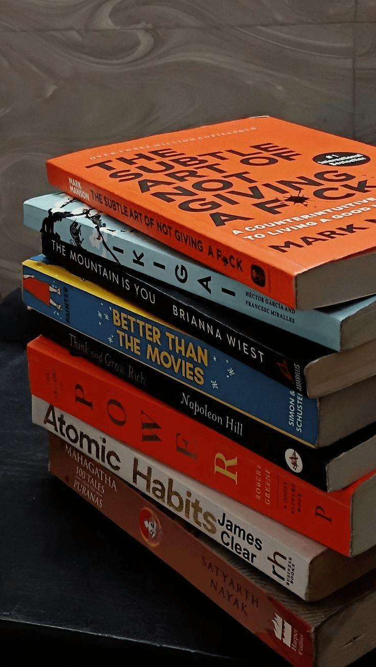 Stack of popular published books including Atomic Habits, The Subtle Art of Not Giving a F*ck, and Ikigai
